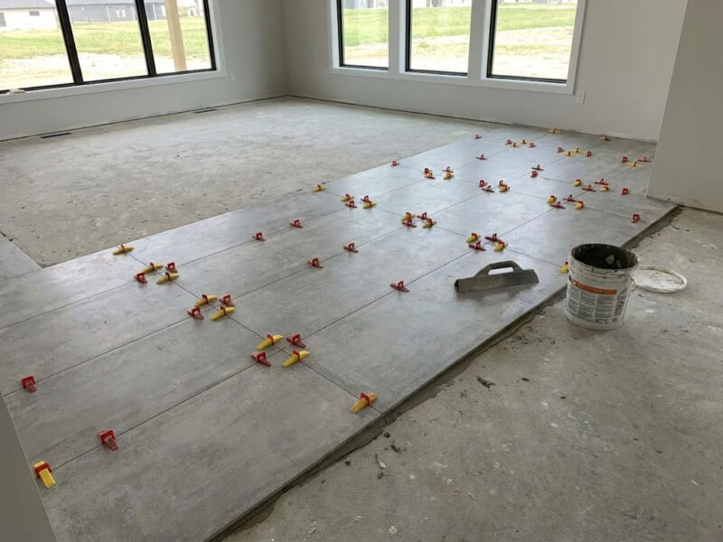 Large Format Flooring Installation. This image demonstrates the scale of a large open-plan living area being tiled with large-format porcelain. A professional leveling system is visible, indicating high-quality workmanship.