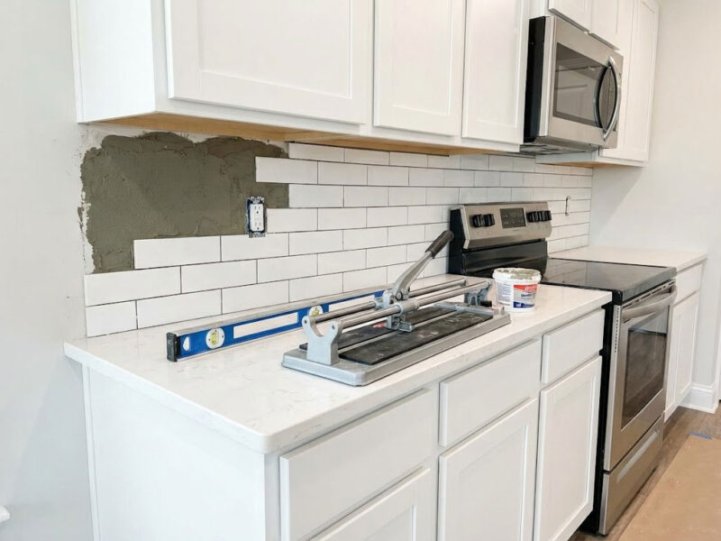 ADU Kitchen Backsplash Installation. A classic subway tile backsplash is being installed in a new kitchen. The mortar on the wall and tools on the counter perfectly illustrate the process.