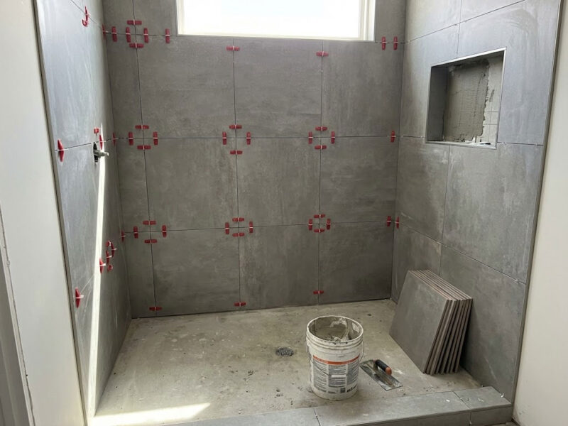 Master Bathroom Shower Installation. This image shows a large, walk-in shower being tiled with large-format porcelain. The use of spacers and the visible tools highlights the precision of the work.