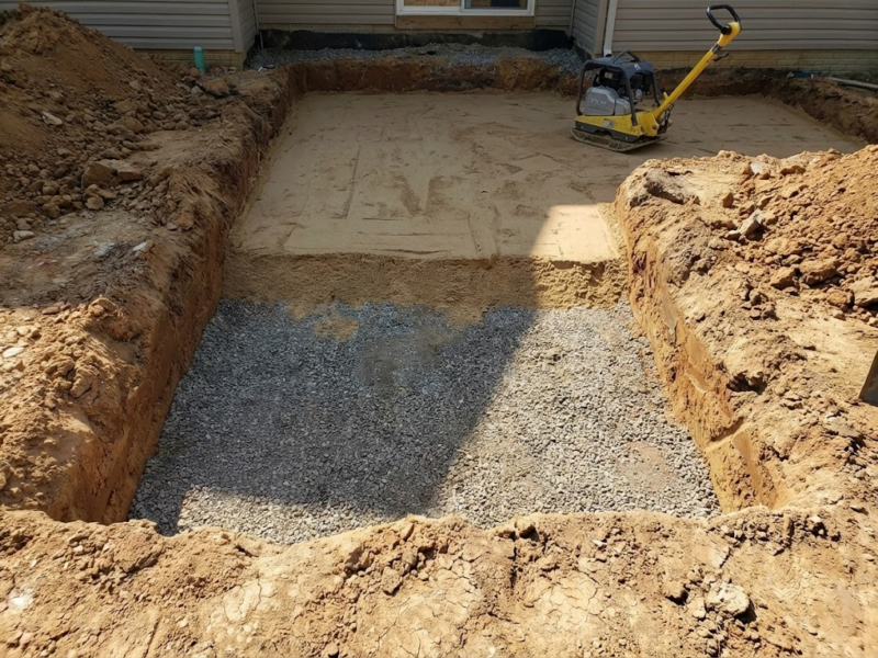 Patio Base Prep: Preparing the foundation for a Charmet Tile paver installation, showing excavation, gravel base, and a plate compactor.