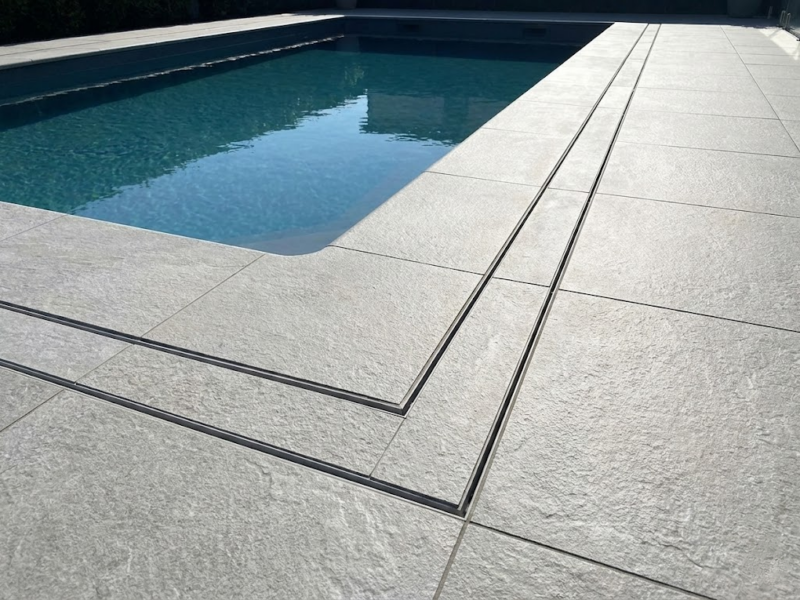 Grey Pool Deck: Grey porcelain pavers by Charmet Tile surrounding a swimming pool with a sleek linear drain feature.